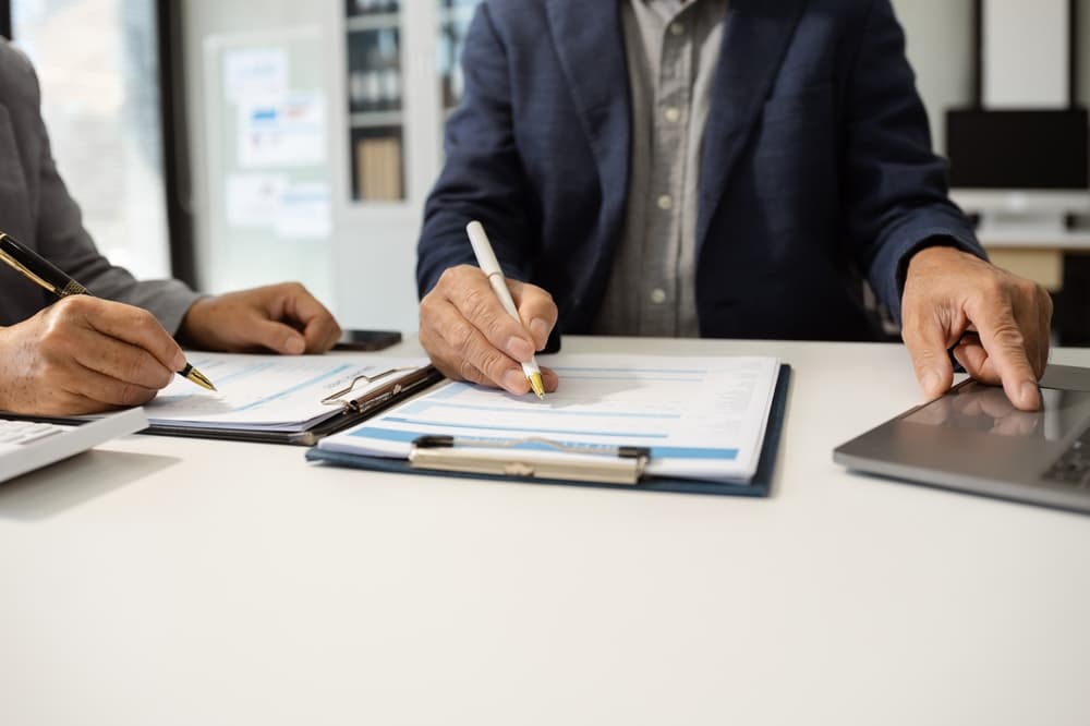 Finance managers meeting in a modern office, utilizing smartphones, laptops, and digital tablets.