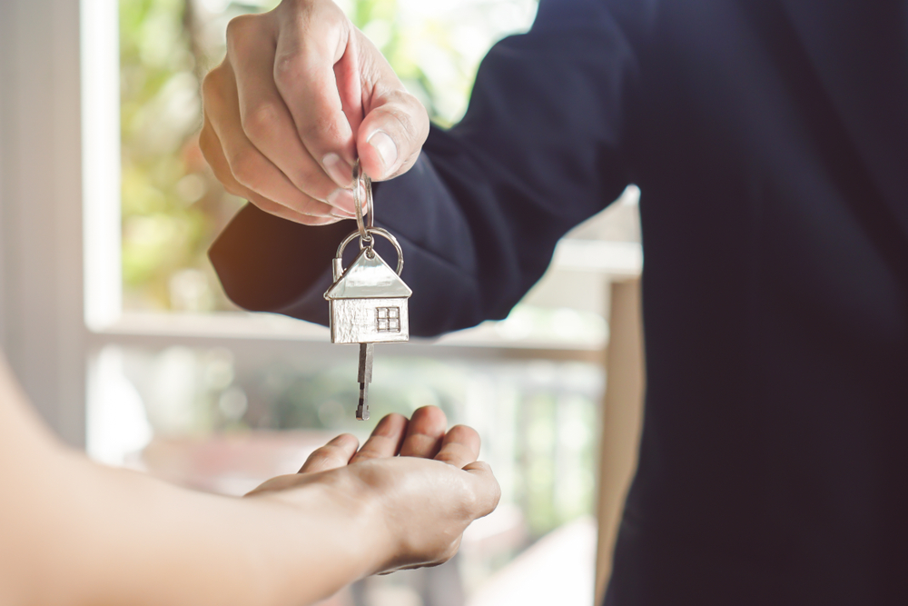 Close-up of a person handing over a house-shaped key to another person's open palm, symbolizing a rental or property agreement.