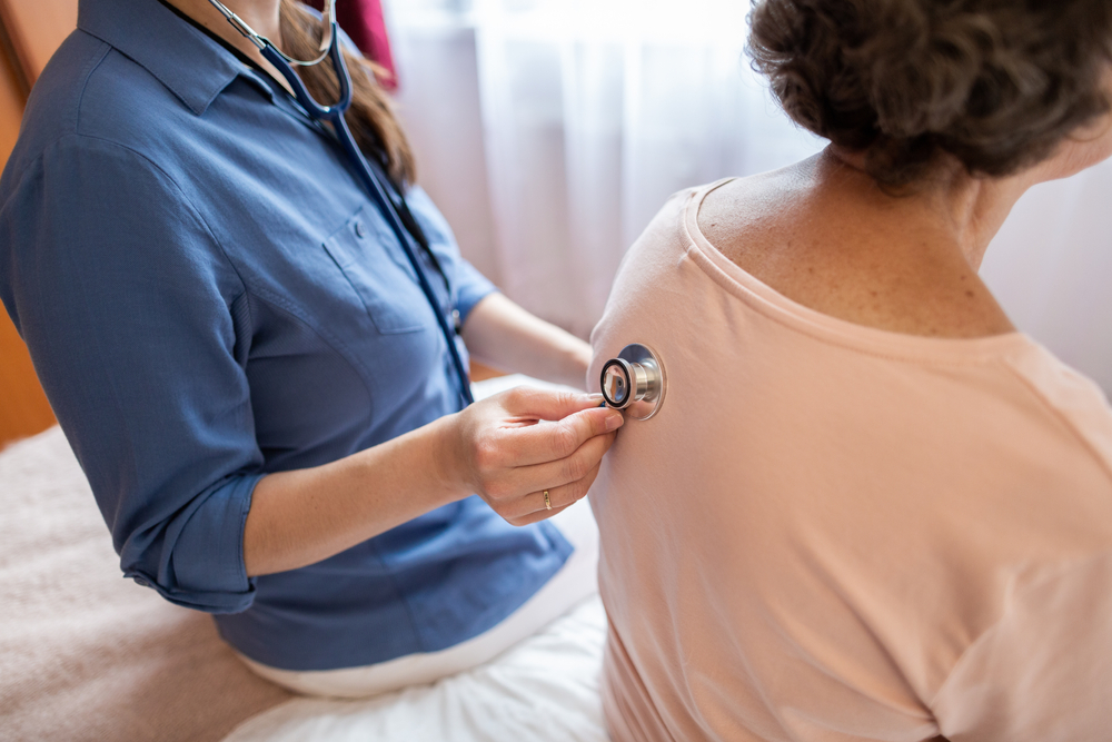 Healthcare provider using a stethoscope to listen to a female patient’s back during a medical exam in a clinical setting.