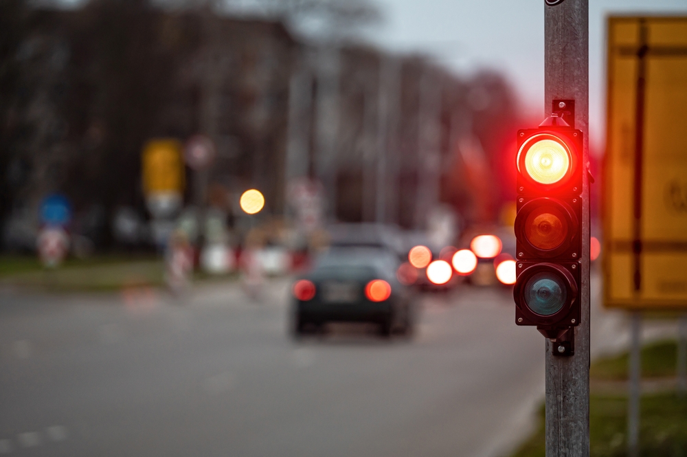 Close-up of a red traffic light at an intersection, with blurred cars and city lights in the background during dusk.